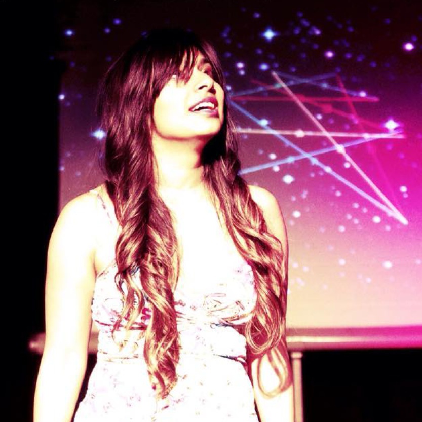 A person is looking up and to the right of the photo. They are wearing a white top with no sleeves. The image is cut off at the waist and the background is a pink gradient with white stars