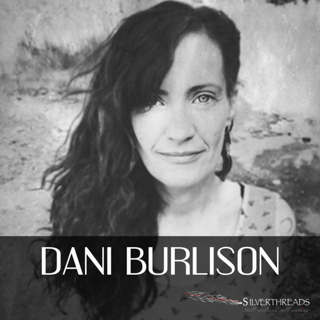 Black and white photo of Dani Burlison. She looks right at the camera with her long dark hair swept towards onside. Behind her is a rocky, textured background. "Dani Burlison" is in white text along the bottom, with the silver threads logo in the bottom right corner.