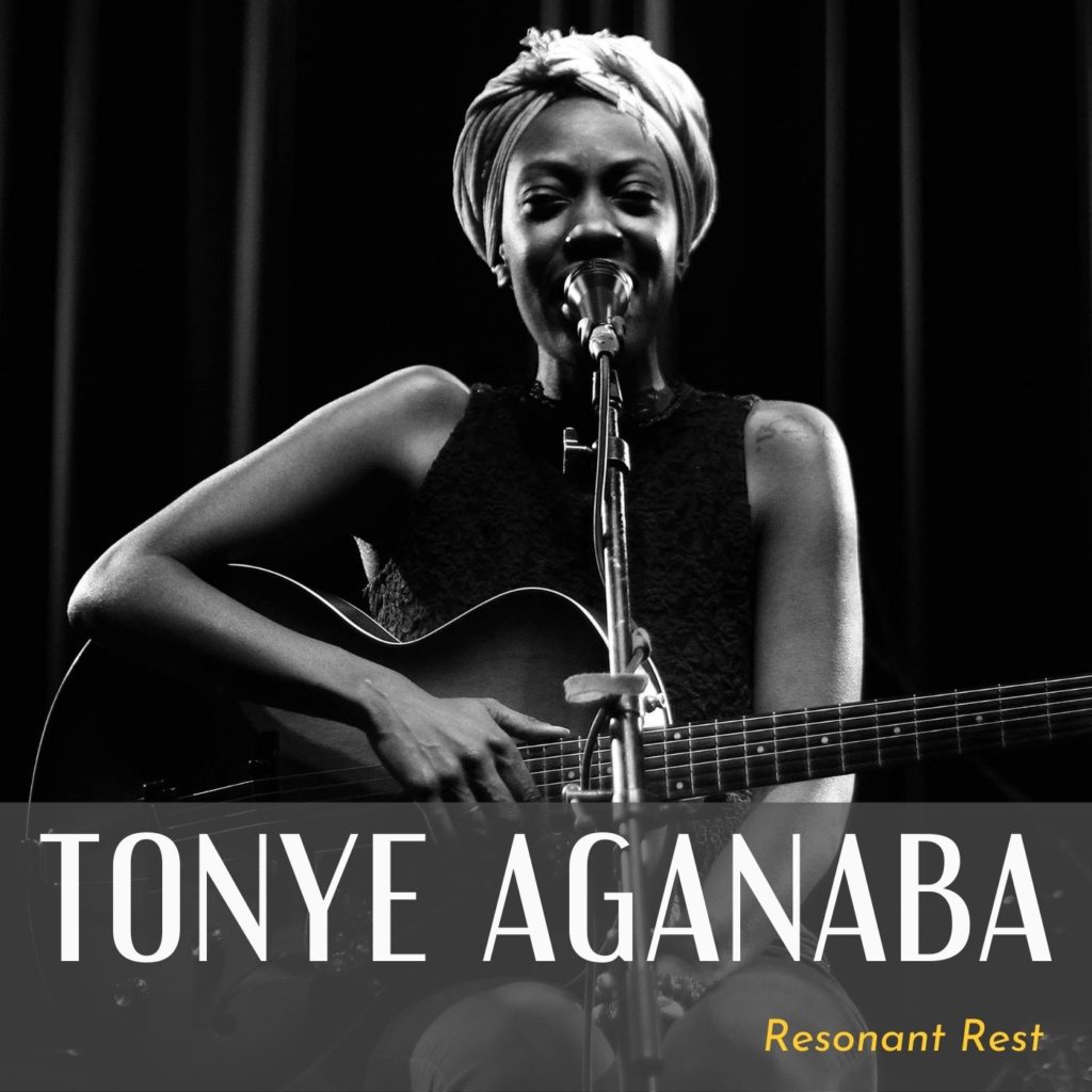 Black and white photo of Tonye Aganaba smiling and sining into a microphone. They are holding a guitar