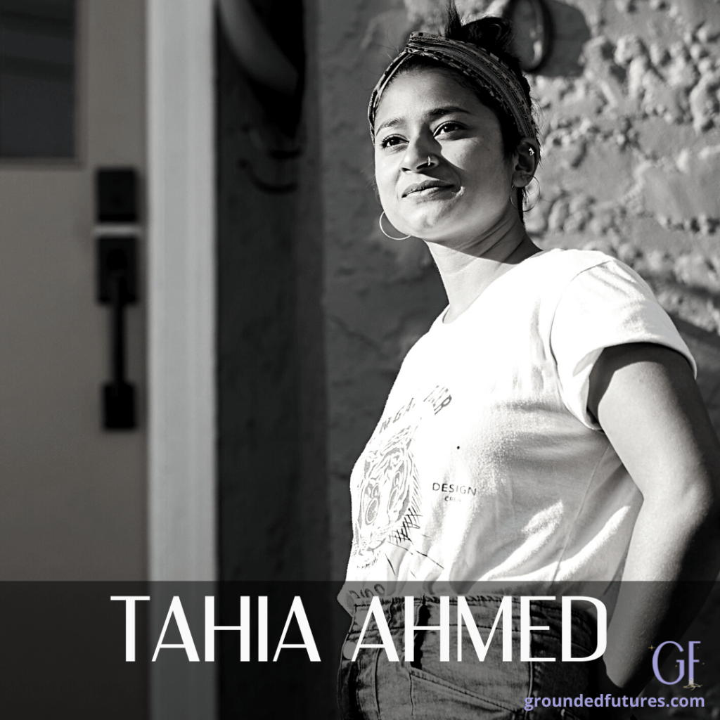 Black and white photo of Tahia Ahmed look off-camera, smiling, wearing a white t-shirt, hoop earrings, a nose ring and a headband with hair up.