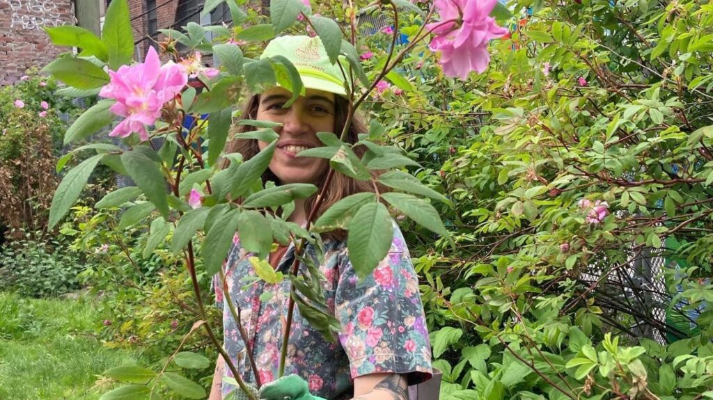 Photo of Sarah obscured behind long stemmed roses in a garden