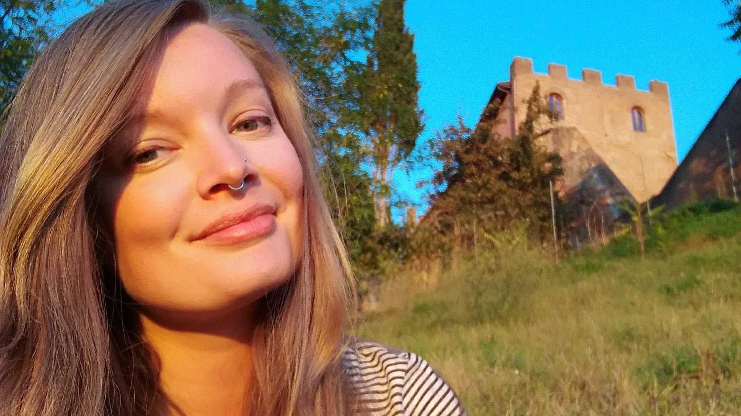 Headshot of Jo smiling at the camera with an old architectural structure in the background